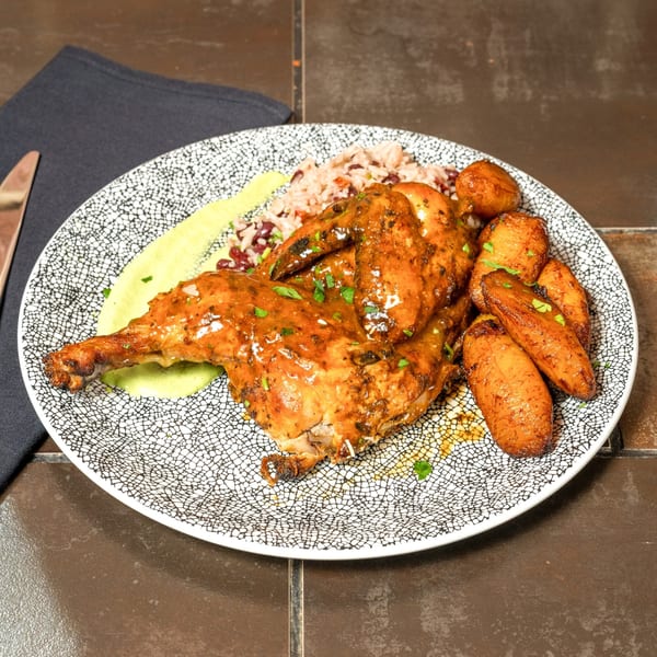 Cuban-style roasted chicken with rice, beans, plantain puree, and glazed carrots on a patterned plate.