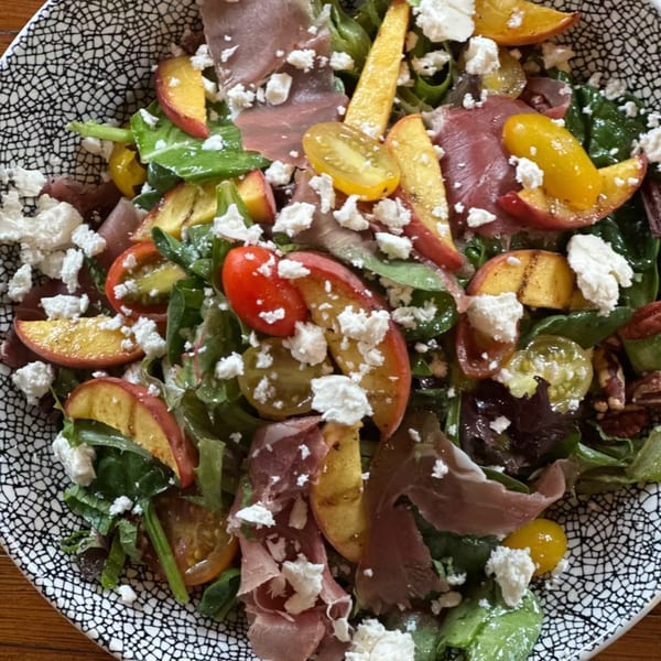 A vibrant salad with prosciutto, grilled peaches, tomatoes, and feta cheese in a patterned bowl.