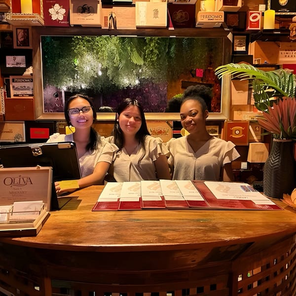 Three Havana 151 staff members smiling behind a wooden reception desk with menus and decor.