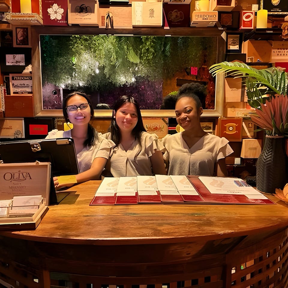 Three Havana 151 staff members smiling behind a wooden reception desk with menus and decor.