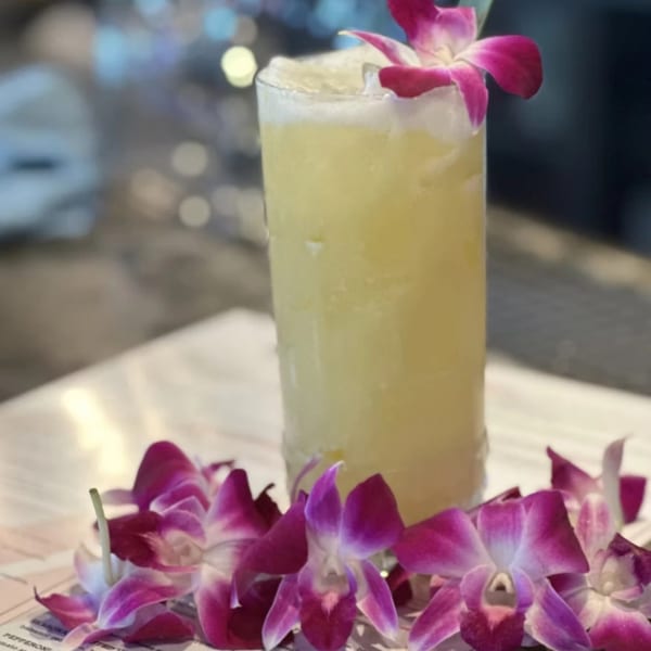Tall yellow cocktail garnished with a purple orchid, surrounded by more orchids on a menu.