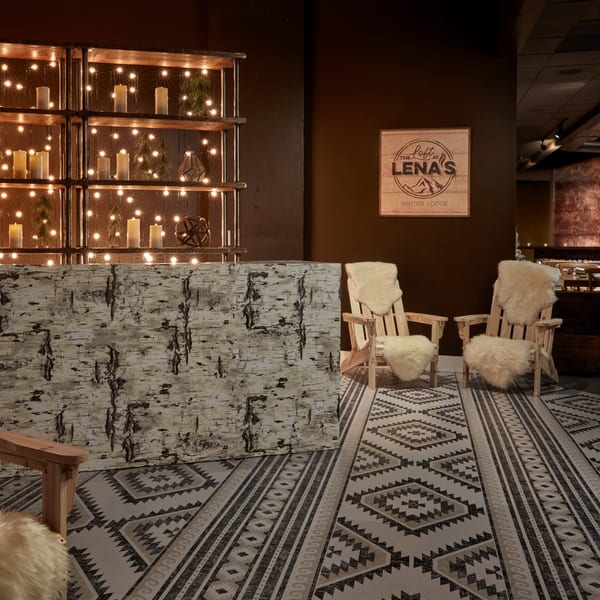 Cozy winter lodge decor with birch-covered bar, Adirondack chairs, string lights, and a patterned rug.