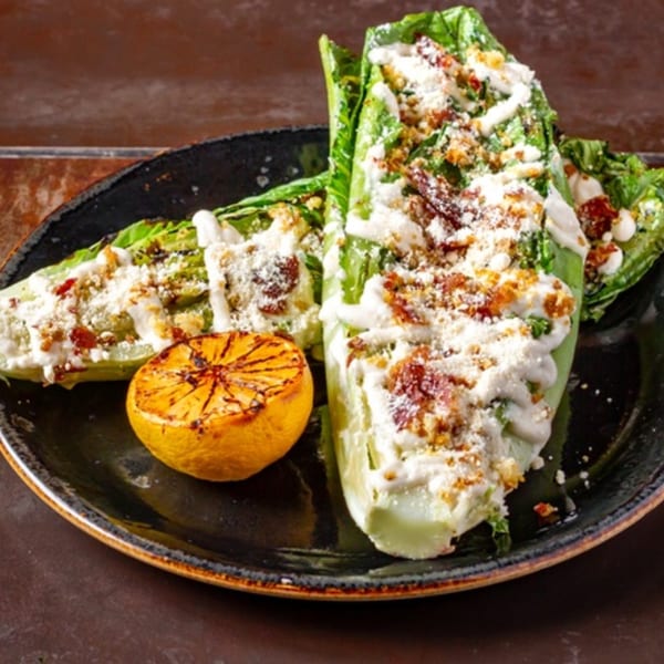 Grilled romaine lettuce hearts with Caesar dressing, parmesan, bacon bits, and a grilled lemon half.