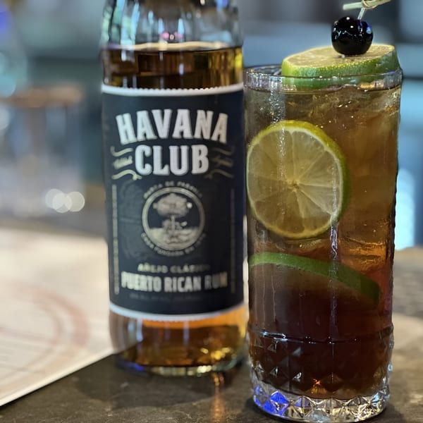 A Havana Club rum bottle next to a tall cocktail garnished with lime and a cherry.
