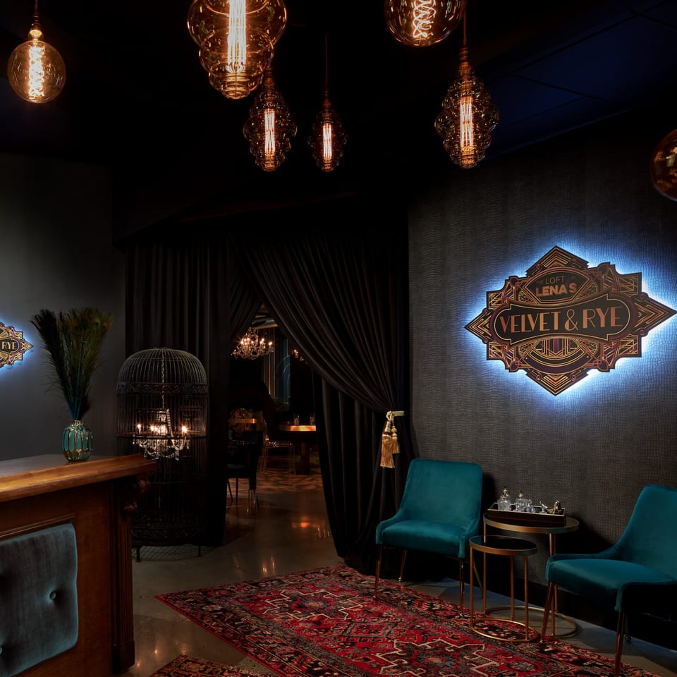Dark, luxurious lounge entrance with velvet chairs, ornate rug, and glowing "Velvet & Rye" sign.