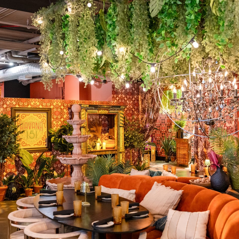 Havana 151 restaurant interior with lush greenery, patterned walls, a fountain, and orange seating.