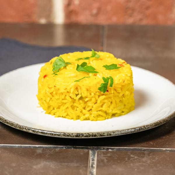 A serving of vibrant yellow Cuban rice, garnished with fresh parsley, on a white plate.