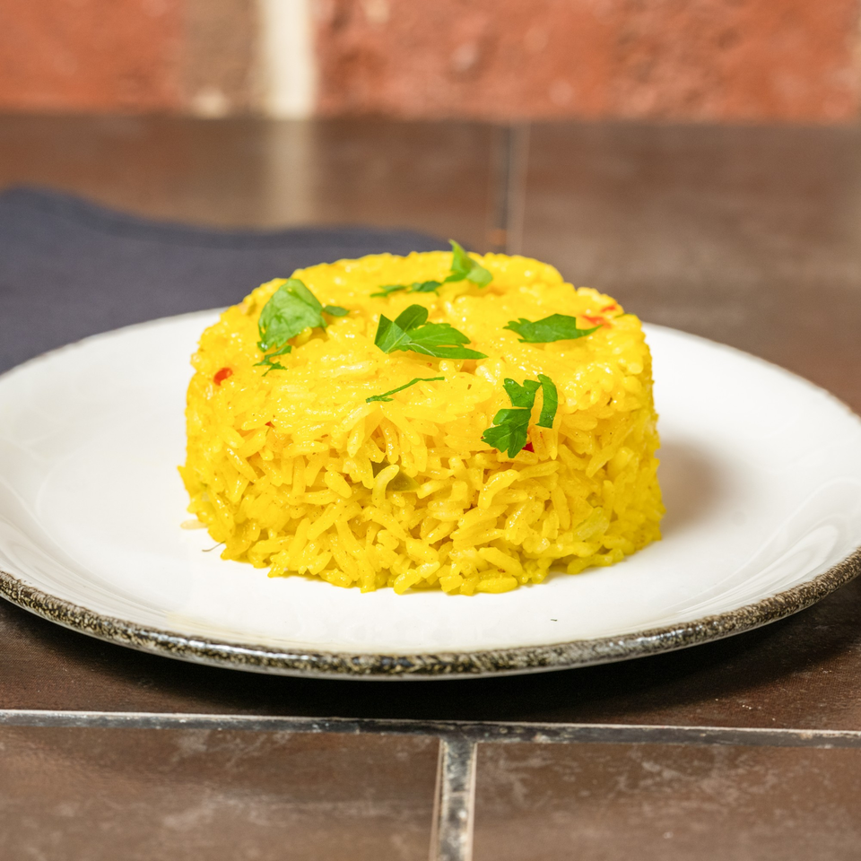 A serving of vibrant yellow Cuban rice, garnished with fresh parsley, on a white plate.