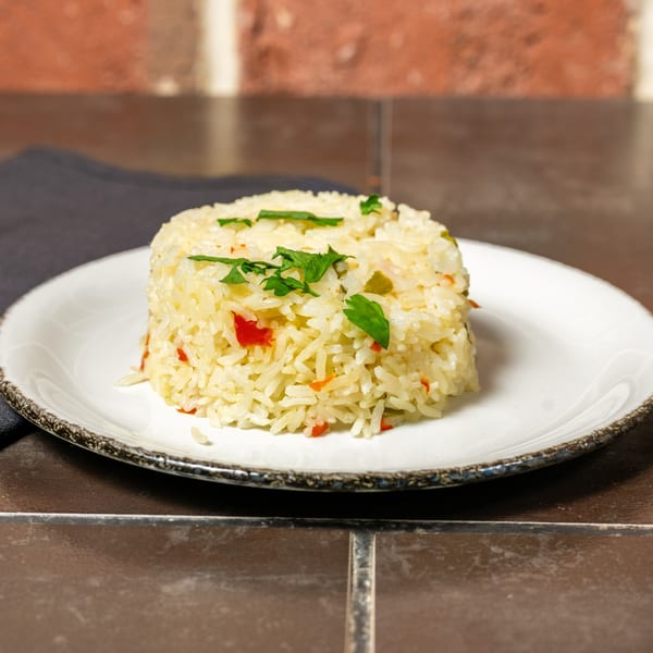 A serving of Cuban yellow rice with red peppers and green herbs on a white plate.