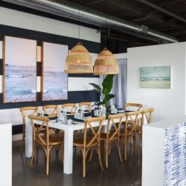 A long white dining table with wooden chairs, wicker lamps, and ocean art on a striped wall.