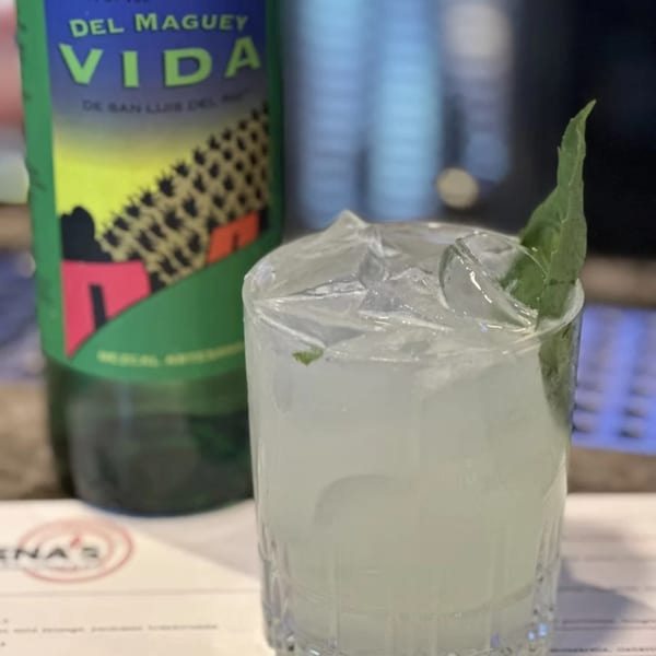 A refreshing mojito with ice and a mint leaf, next to a bottle of Del Maguey Vida.