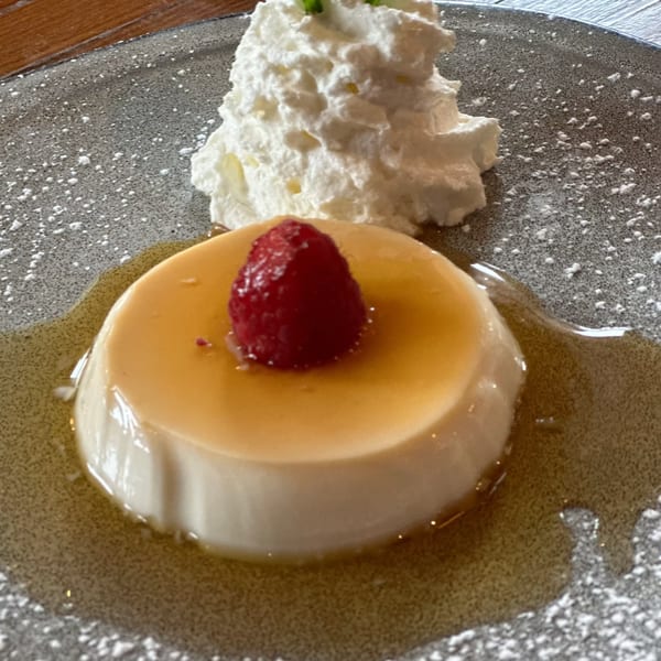 Cuban flan dessert with caramel sauce, a raspberry, and whipped cream on a speckled plate.