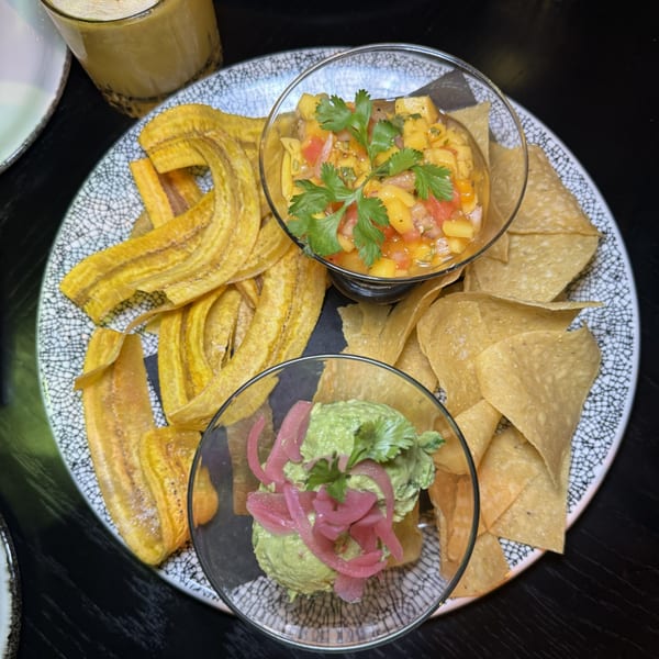 A plate of plantain chips and tortilla chips with bowls of mango salsa and guacamole.