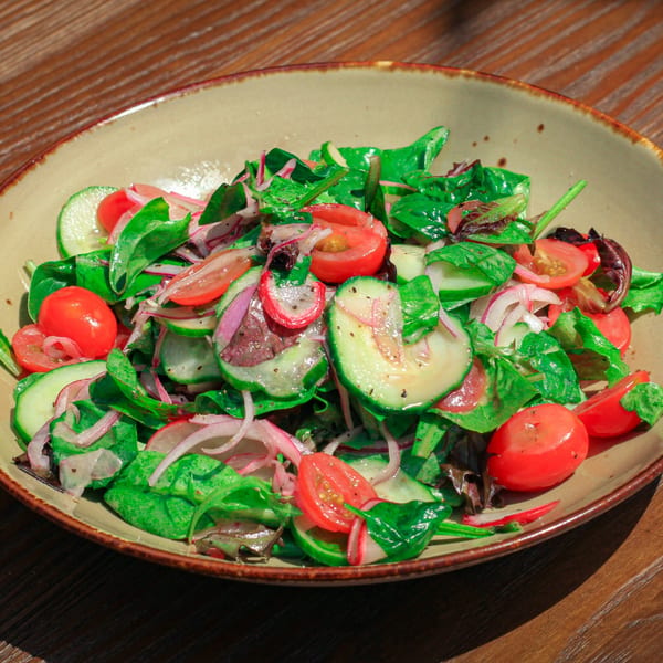 A fresh salad with mixed greens, sliced cucumbers, cherry tomatoes, and red onions in a bowl.