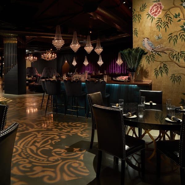 Dark, luxurious Havana 151 dining room with chandeliers, bar, and gold floral wall mural.