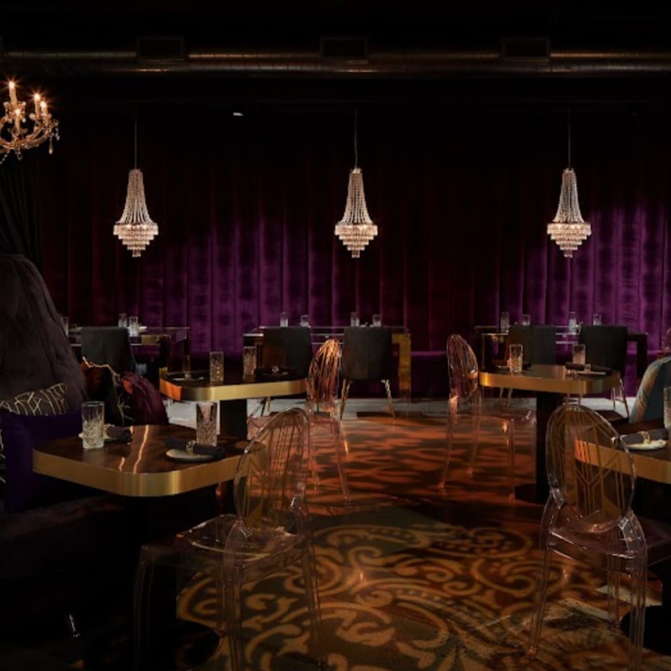 Elegant dining room at Havana 151 with purple velvet curtains, crystal chandeliers, and gold tables.