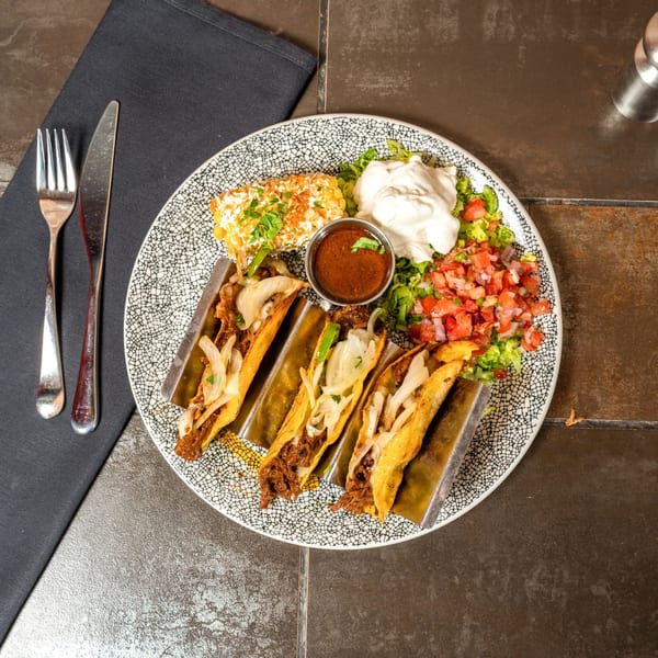Four Havana 151 tacos with elote, salsa, and sour cream on a patterned plate.