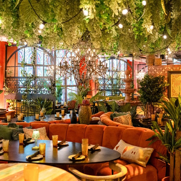 Havana 151 restaurant interior with lush greenery, string lights, chandeliers, and orange banquette seating.