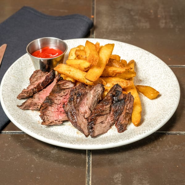 Grilled skirt steak slices with a side of golden french fries and a cup of ketchup.