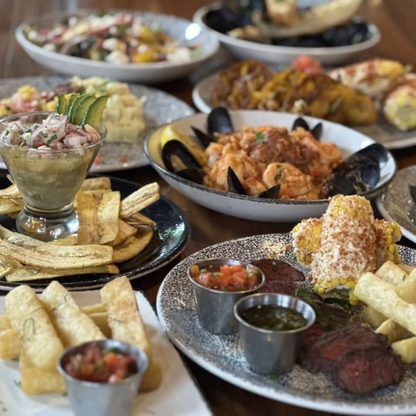 A table full of Cuban dishes, including ceviche, plantain chips, paella, and steak with corn.